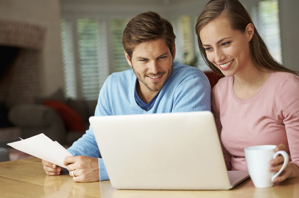 A young couple looking at a laptop researching new home warranties and construction builders.
